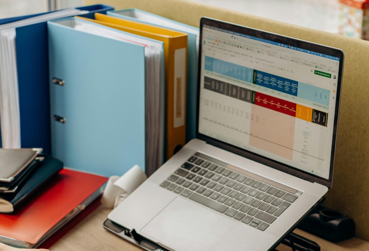 Laptop displaying tabulated survey data in a spreadsheet beside binders of project files